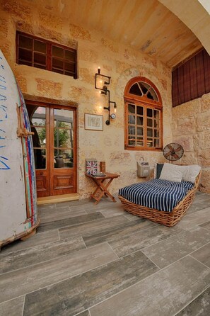 A rustic room with a bed, a fan, a small table, and a door. - Luxury "House of Character" Golden Bay/Manikata. (Mellieha)