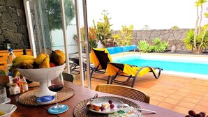Un espace extérieur aménagé pour les repas, avec une piscine, des meubles en osier et un mur en pierre.