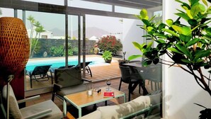 Une chambre avec vue sur une piscine, une table en verre avec un verre de vin et une plante en pot.
