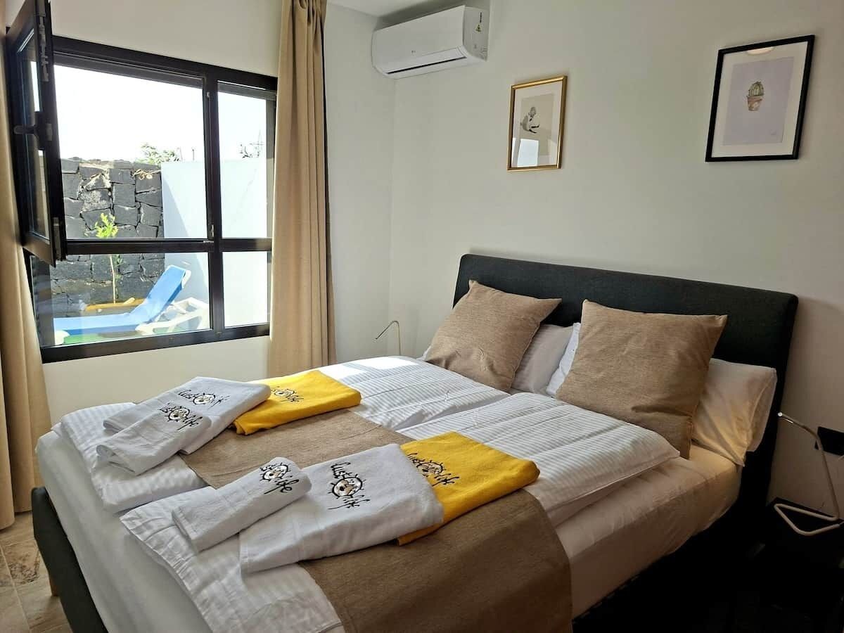 A hotel room with a bed, a window with a view of the outside, and a wall-mounted air conditioner.