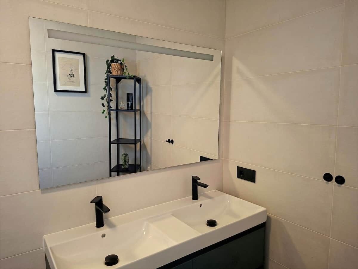 Une salle de bain avec un double lavabo, un grand miroir et une étagère contenant des articles de toilette.