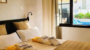 Hotelkamer met een bed, kussens, een raam met uitzicht op een zwembad, en een lijst met een foto aan de muur.