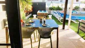 Een terras met een eettafel en stoelen, een jacuzzi en een zwembad op de achtergrond.