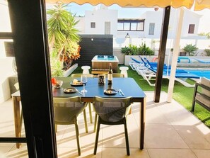 Een terras met een eettafel en stoelen, een jacuzzi en een zwembad op de achtergrond.