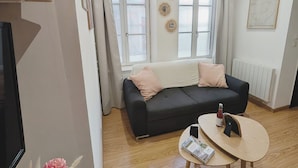A living room with a black sofa, a round wooden coffee table, and a window with blinds. - Cosy studio at the foot of the ramparts (Boulogne-sur-Mer)