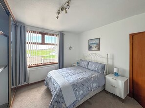 Ein Schlafzimmer mit Bett, Nachttisch, Fenster mit Ausblick und einem Bild an der Wand.