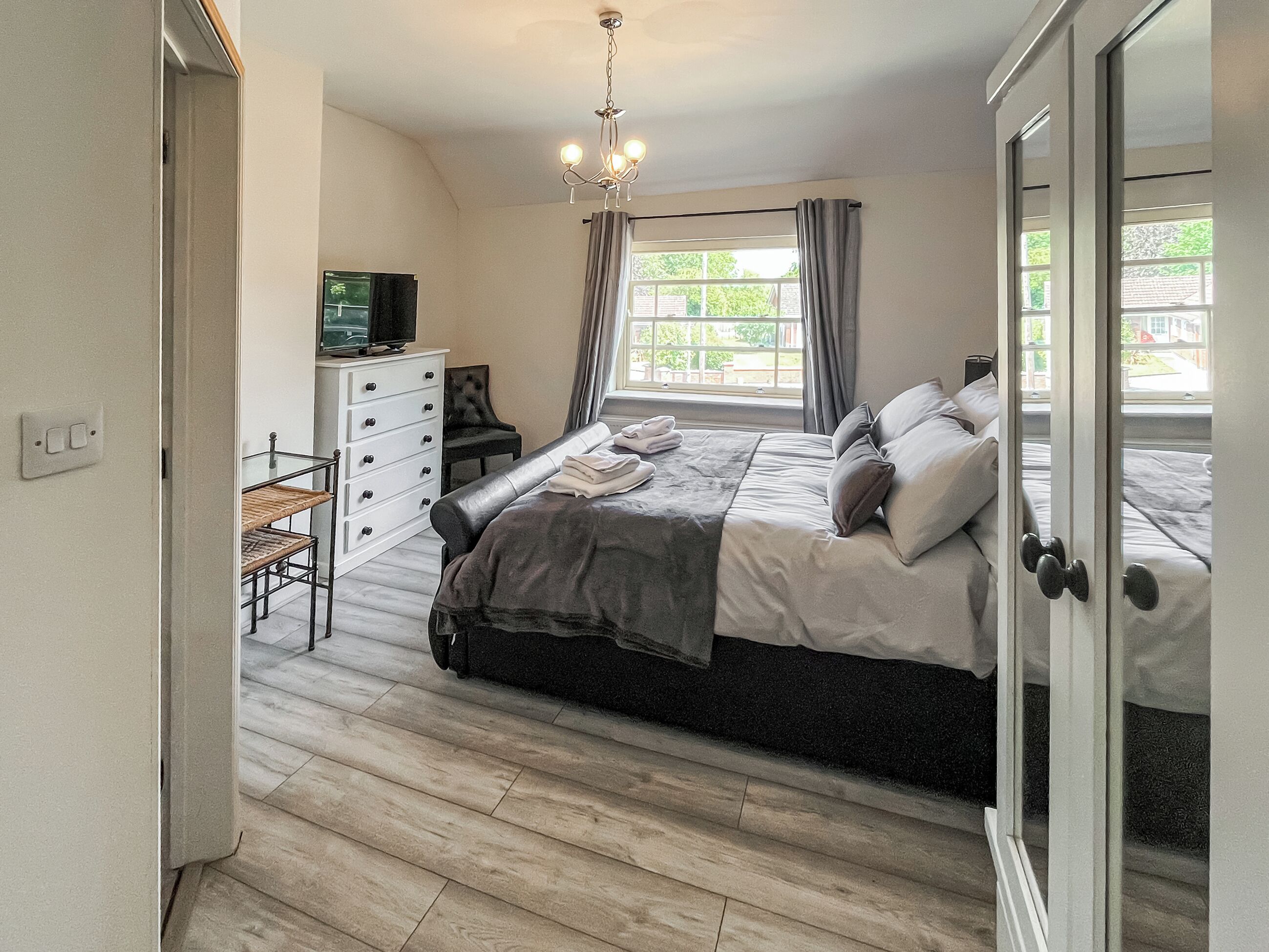 Une chambre à coucher avec un lit, une commode, un téléviseur et une fenêtre avec des rideaux.