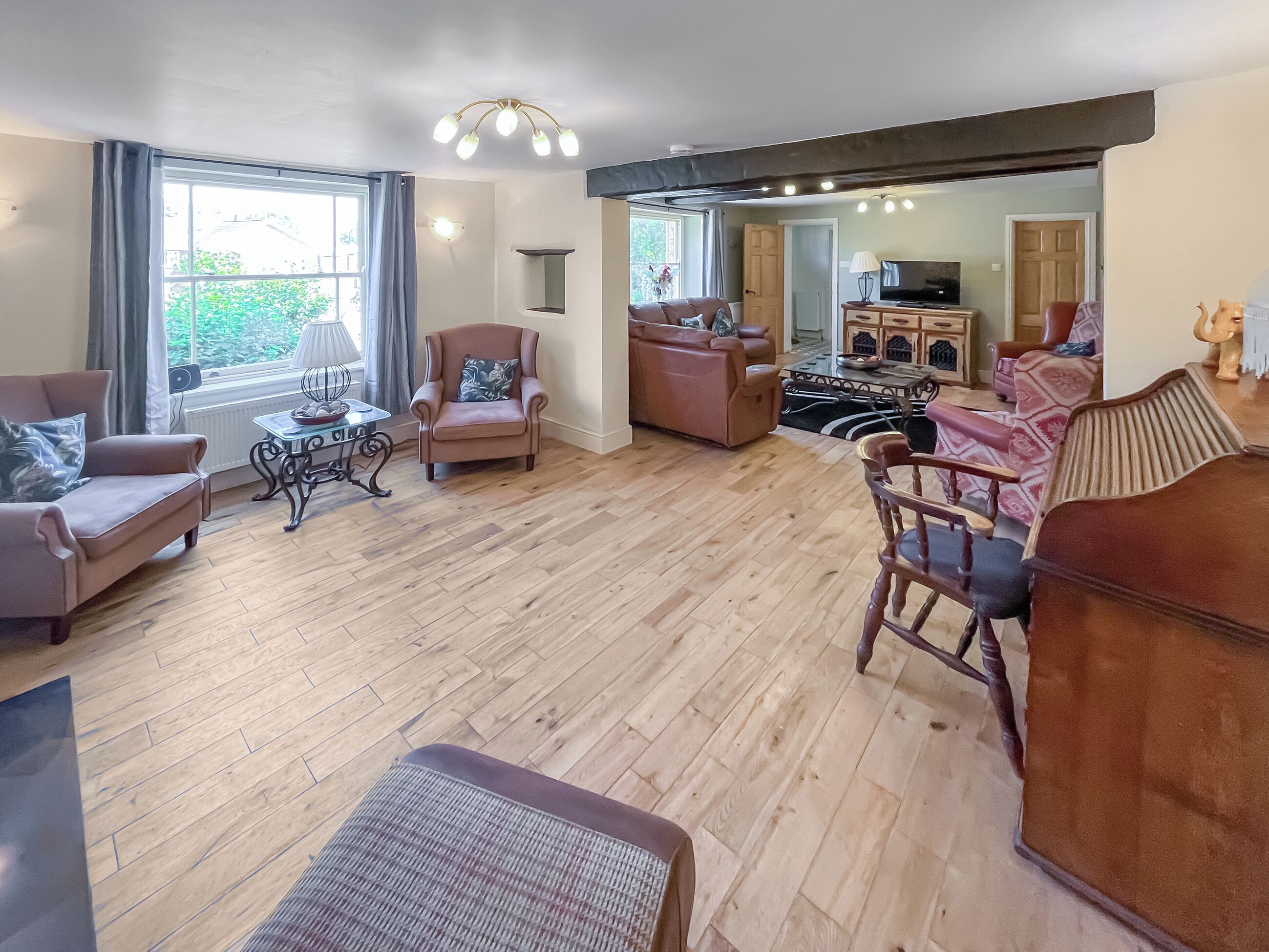 A spacious living room with a wooden floor, a sofa set, a coffee table, and a television.