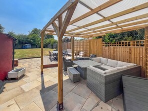 Un patio couvert agrémenté d’une pergola en bois, de mobilier d’extérieur et offrant une vue sur le jardin arrière.