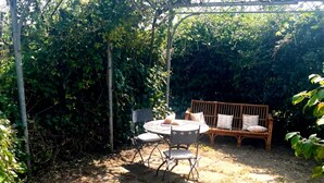Un jardin agrémenté d’une pergola, d’une table ronde, de deux chaises et d’un canapé en osier.
