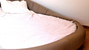 Un lit simple avec une tête de lit beige, une couvre-lit blanche et une lampe fixée au mur.