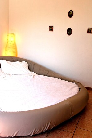 Ein Einzelbett mit beigem Kopfteil, einer weißen Bettdecke und einer Wandlampe.
