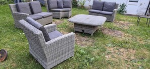 Ein Set aus Rattangemöbeln für den Außenbereich mit einer Couch, zwei Sesseln und einem Couchtisch, angeordnet auf einer Rasenfläche.