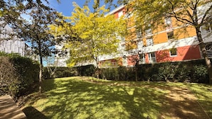 A well-maintained courtyard with a lawn, trees, and a building with red and white exterior walls. - Apartment + Parking in Paris, Massy (TGV/RER B/C, Orly Bus) (Massy)