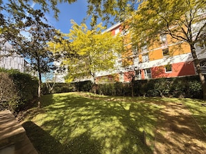 Un pati ben cuidat amb gespa, arbres i un edifici amb parets exteriors vermelles i blanques.