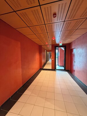 A corridor with red walls, white tiled floor, and a ceiling with ventilation ducts.