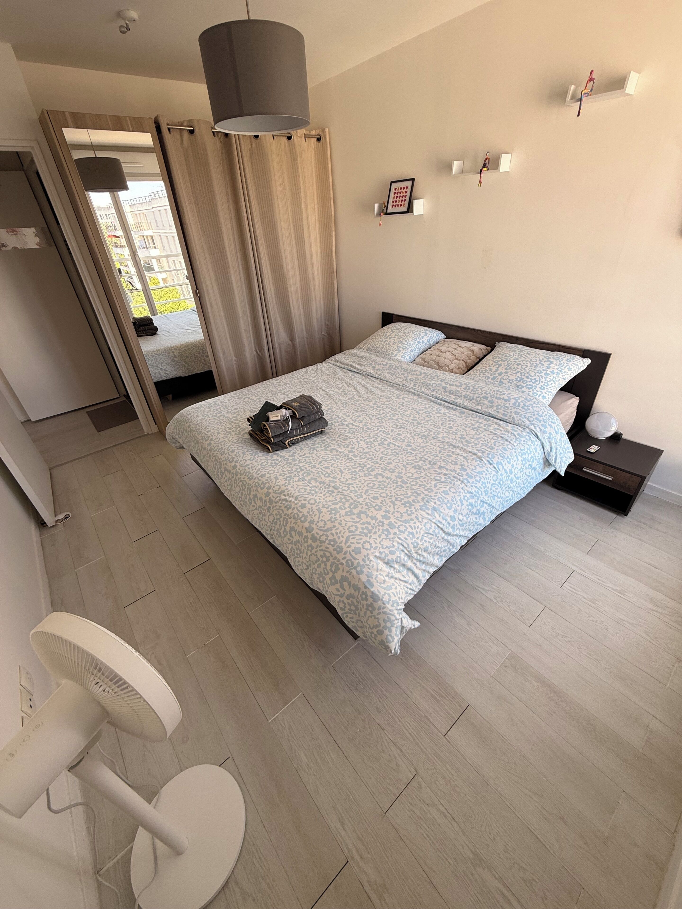 Une chambre à coucher moderne avec un lit, une table de chevet et un ventilateur sur pied.