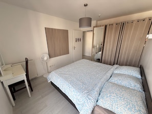 A bedroom with a bed, a bedside table, a mirror, a radiator, and a window with curtains.