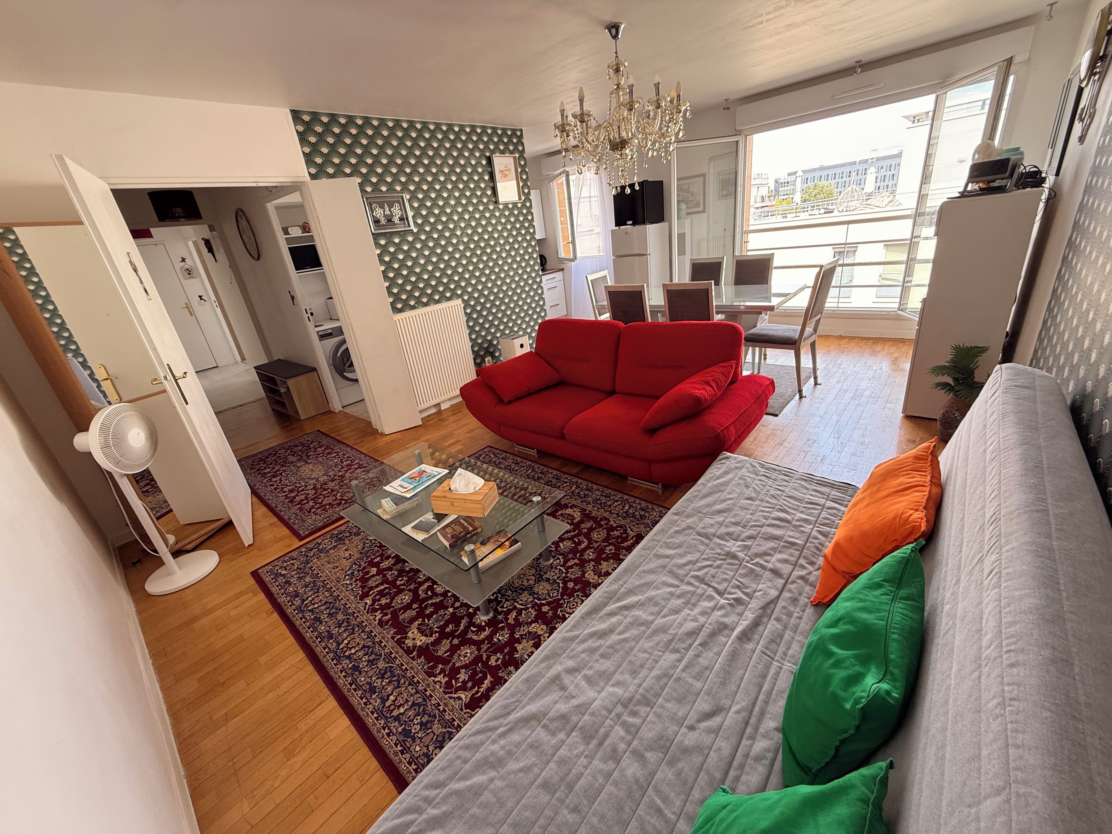 A modern living room with a red sofa, a grey sofa, a glass coffee table, and a patterned rug.