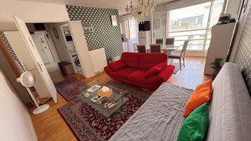 A modern living room with a red sofa, a grey sofa, a glass coffee table, and a patterned rug.