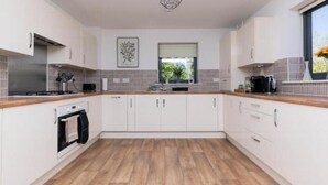 A modern kitchen with white cabinets, a wooden countertop, a built-in oven, and a window with a view of greenery. - Stylish 2-Bed Flat with Parking Near Tube & Heathrow (Uxbridge)