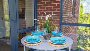 A table set with blue plates, silverware, and wine glasses, with a plant centerpiece, against a brick wall and glass door. - Stylish 2-Bed Flat with Parking Near Tube & Heathrow (Uxbridge)