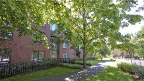 A brick building with a paved walkway and a tree-lined path. - Stylish 2-Bed Flat with Parking Near Tube & Heathrow (Uxbridge)