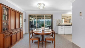 A dining area with a wooden table and chairs, a cabinet with glass doors, and a view through a glass door to a balcony.