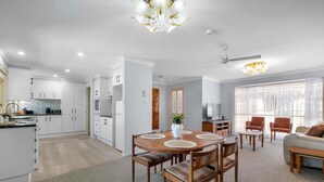 A modern kitchen with white cabinets, a dining area with a round table, and a living room with a sofa and chairs.