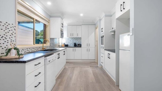A modern kitchen with white cabinetry, a black countertop, and a tiled backsplash.
