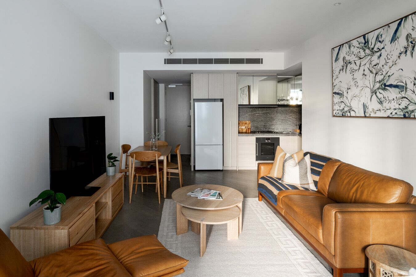 Ein modernes Wohnzimmer mit Fernseher, Ledersofa, Couchtisch und einem Essbereich mit Stühlen und Tisch.