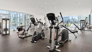 Une salle de sport moderne équipée de divers appareils d’exercice, dotée de grandes fenêtres et offrant une vue sur la ville.