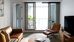 Un salon moderne comprenant un canapé, un fauteuil, une table basse, un téléviseur et un balcon avec une table et des chaises.