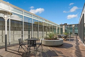 An outdoor patio area with tables and chairs, a planter with plants, and a glass building facade. - Premium St Kilda Rd Apt Pool, Gym and Park Access (St Kilda)