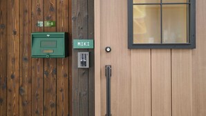 Een houten deur met een naambordje, een groene brievenbus en een raam met uitzicht.