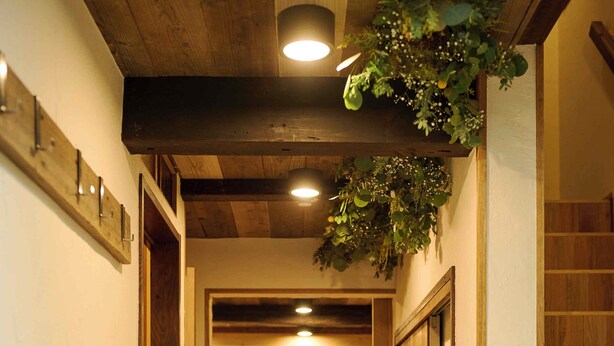 Een houten gang met een eetgedeelte in de verte, houten vloeren en een plafond met inbouwverlichting.