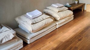 Een kamer met meerdere matrassen tegen een muur gestapeld, een houten vloer en een klein tafeltje met een plant.