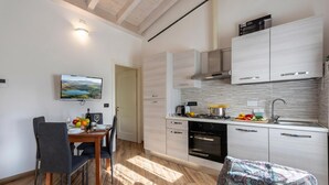 A modern kitchen with a dining area, featuring a TV, wooden flooring, and a patterned cushion. - Via Chiappori Sestri Ponente (Genoa)