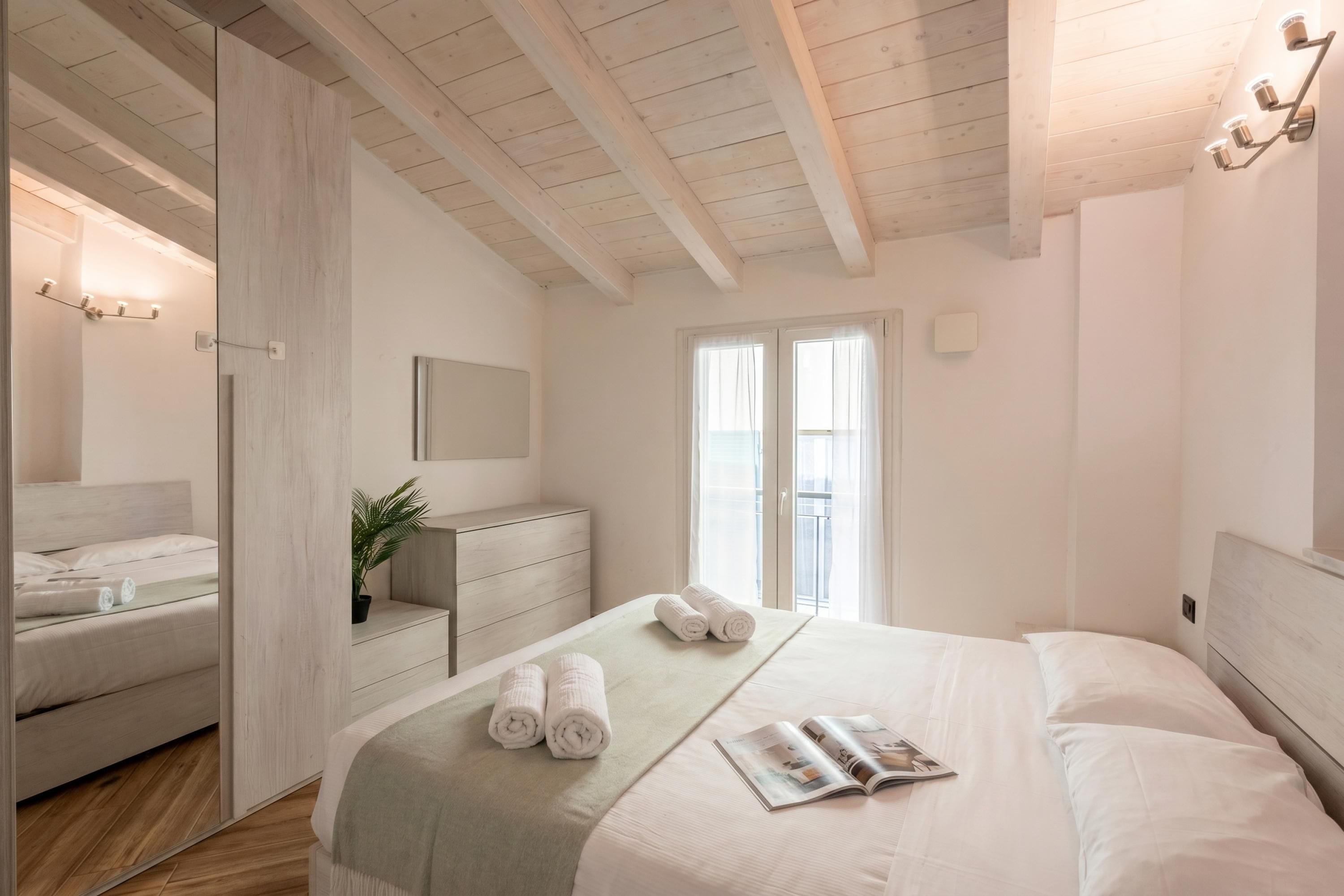 A bedroom with a bed, a dresser, a mirror, and a window.