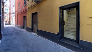 A narrow alleyway with a yellow building, closed shutters, and a visible staircase leading to an upper floor. - Via Chiappori Sestri Ponente (Genoa)