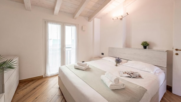A bedroom with a wooden ceiling, a bed with white linens, a bedside table, and a window with curtains. - Via Chiappori Sestri Ponente (Genoa)