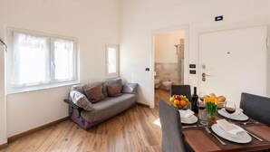A modern living room with a sofa, dining table set for two, and a kitchen in the background. - Via Chiappori Sestri Ponente (Genoa)
