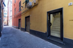 A narrow alleyway with a yellow building, closed shutters, and a visible staircase leading to an upper floor. - Via Chiappori Sestri Ponente (Genoa)