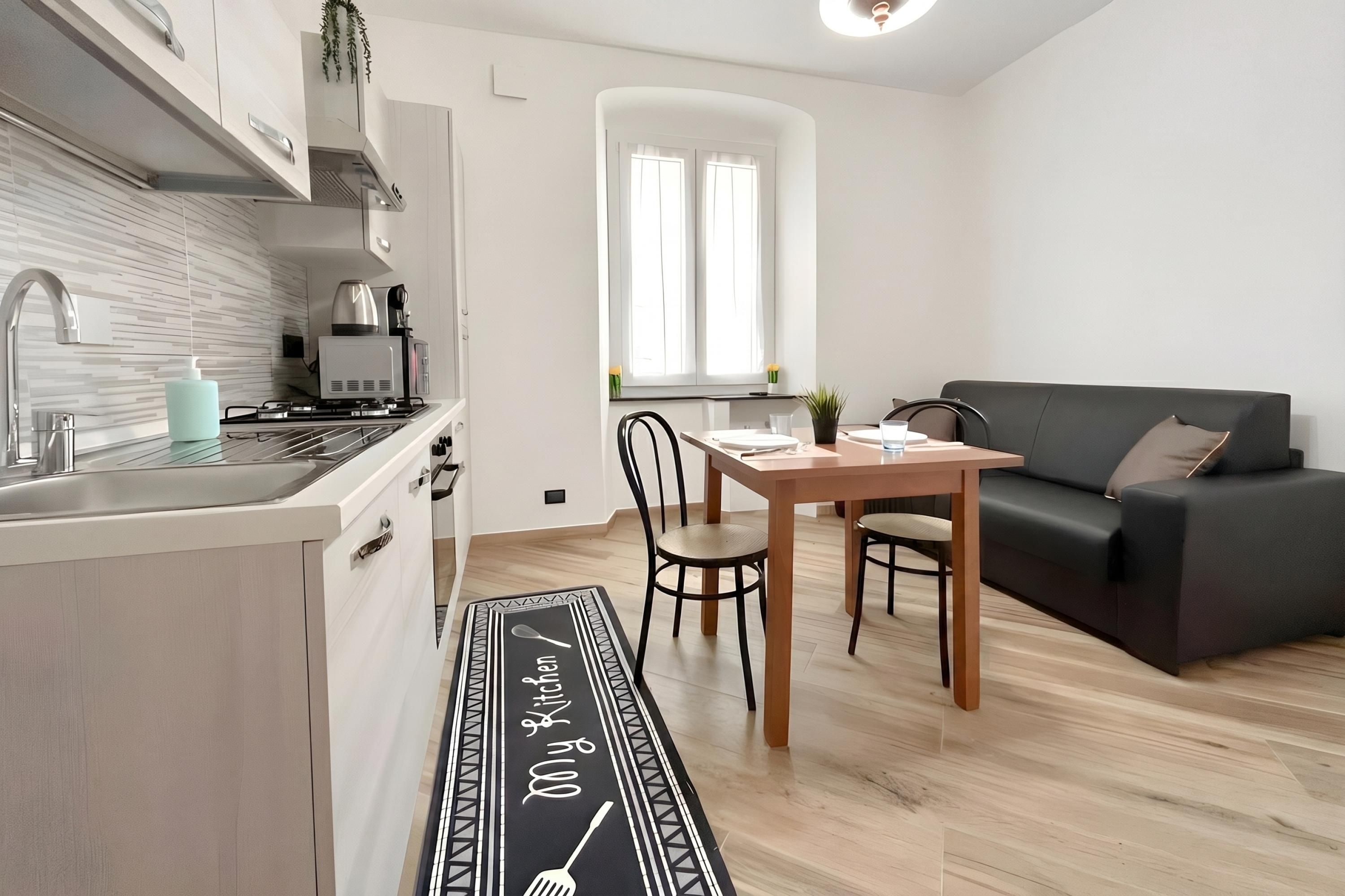 Eine moderne Küche mit Einbauherd, Spüle und Kaffeemaschine. Ein Essbereich mit Tisch und Stühlen sowie ein schwarzes Sofa mit Kissen.