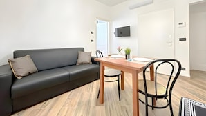 Ein modernes Wohnzimmer mit einer schwarzen Couch, einem Holzesstisch und einem an der Wand befestigten Fernseher.