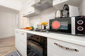 Una cocina moderna con microondas, estufa y horno integrados, una encimera con tabla de cortar y verduras, y una cafetera.