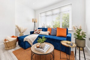 Un salon moderne avec un canapé bleu, une petite table ronde et un lampadaire.