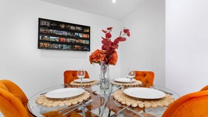 Ein runder Glastisch mit weißen Tellern, orangefarbenen Stühlen und einer Blumenvase.