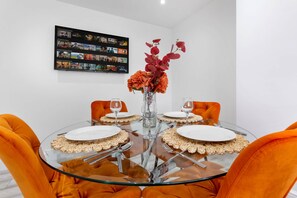 Ein runder Glastisch mit weißen Tellern, orangefarbenen Stühlen und einer Blumenvase.
