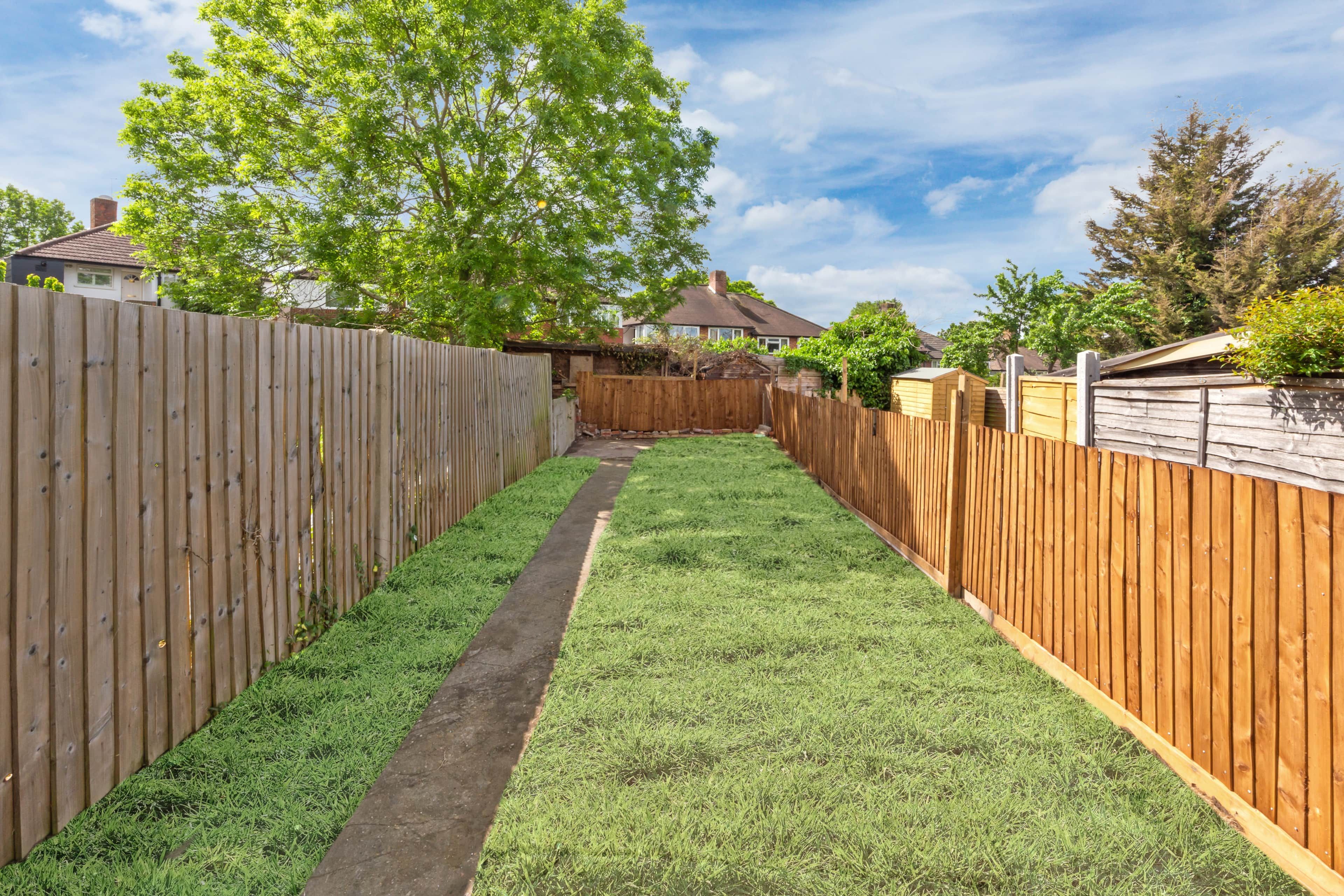 A narrow backyard with a wooden fence, a grassy path, and a tree.